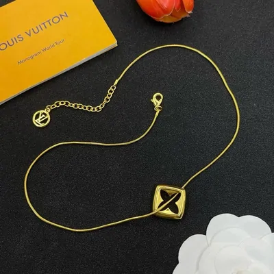 A gold chain necklace with a square pendant, laid on a black tray