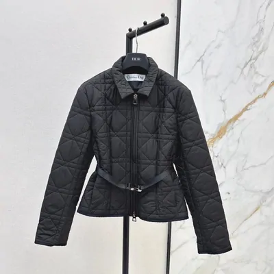 A black quilted jacket hanging on a rail against a marble wall